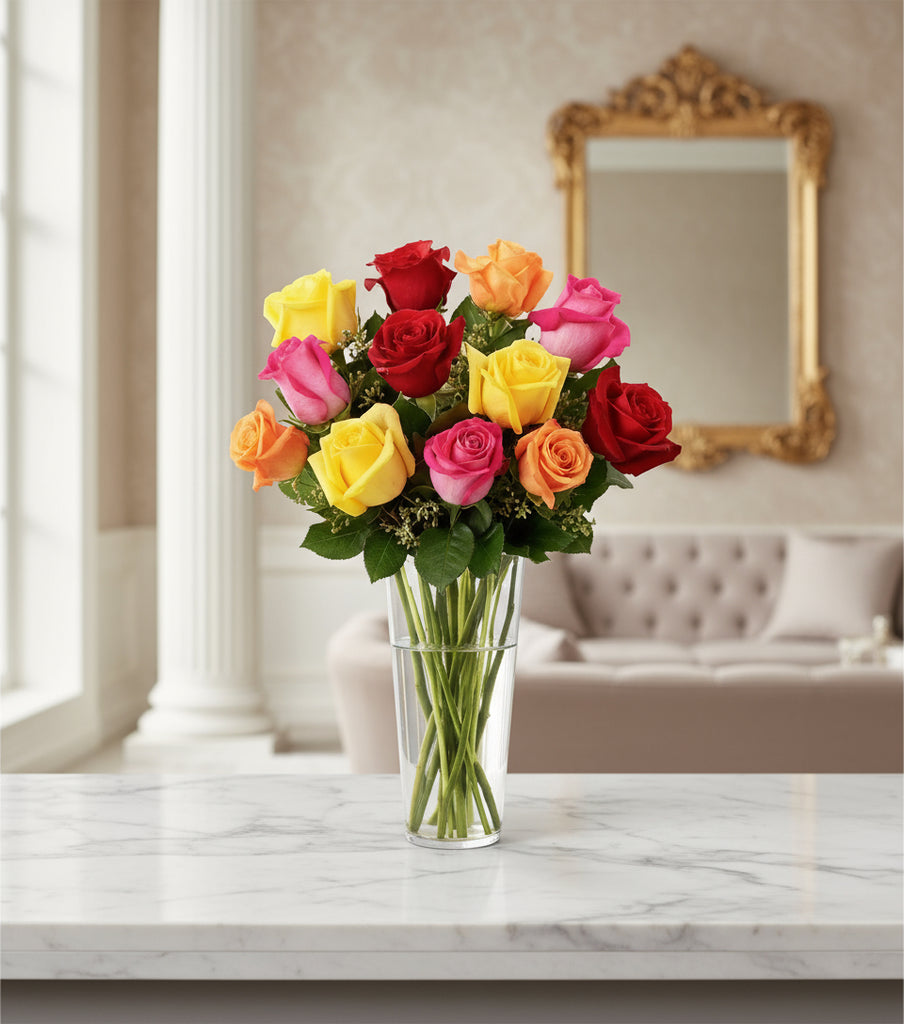 Bouquet of colorful mix roses in a clear vase on a marble surface with a decorative mirror in the background.