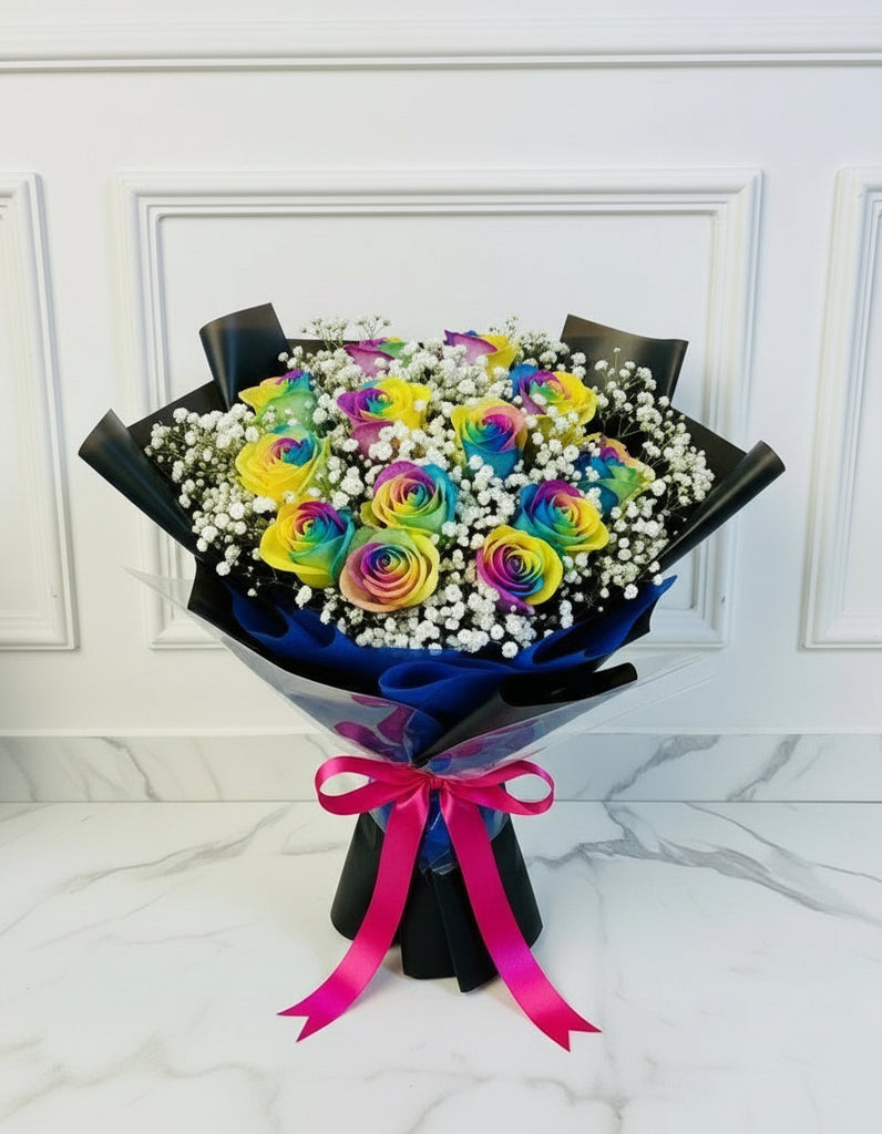 Bouquet of rainbow roses wrapped in black paper with a pink ribbon on a white marble surface.
