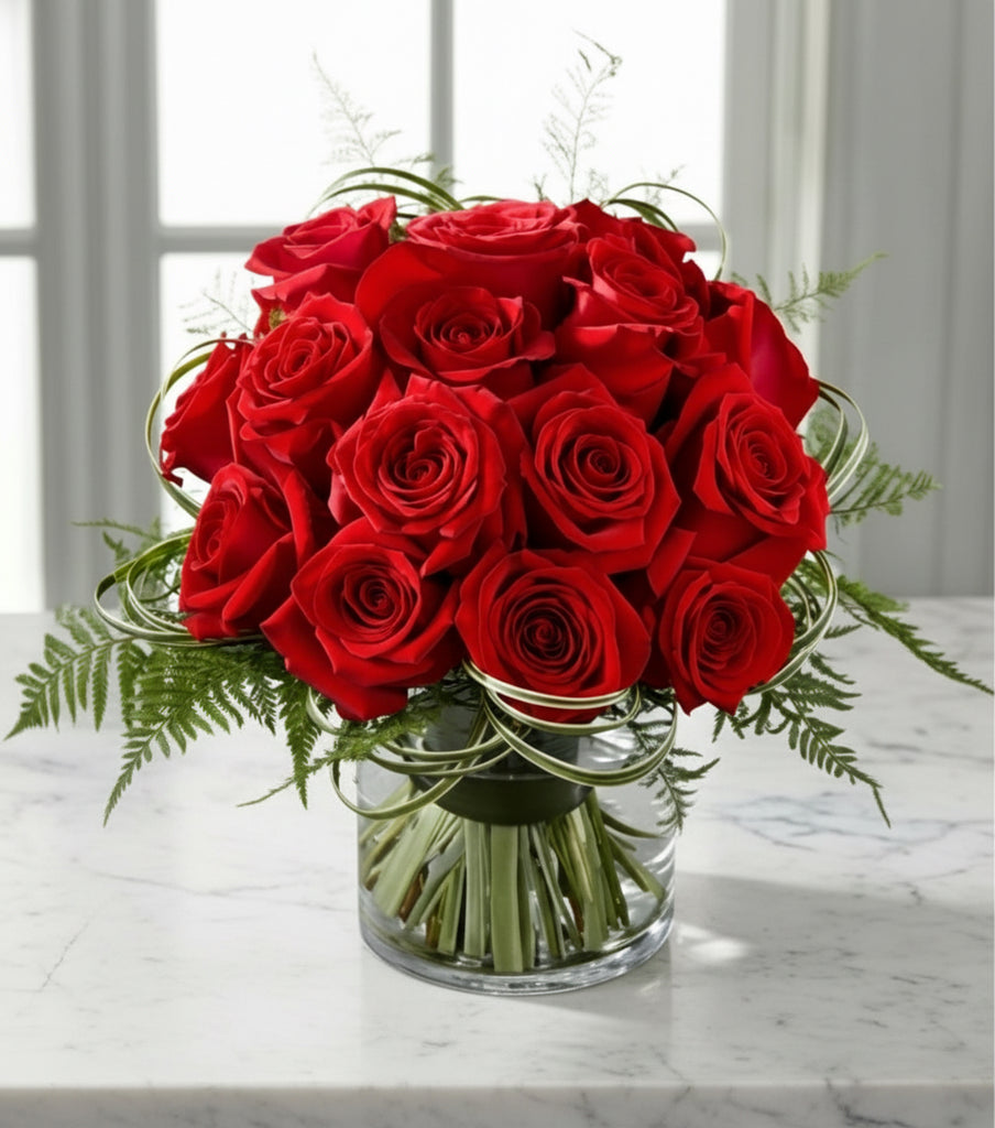 Bouquet of red roses in a clear vase on a marble surface with a window in the background