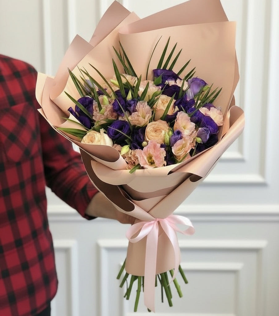 Bouquet of mix flowers wrapped in pink paper with a pink ribbon, held by a person wearing a red plaid shirt.