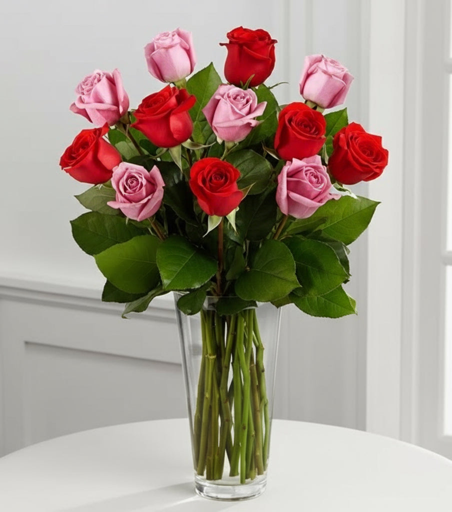 Bouquet of red and pink roses in a clear vase on a white surface with a light gray background.